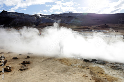 Tourist in volcanic area, Iceland. Boiling mudpots in the geothermal area Hverir and cracked ground around. Location: geothermal area Hverir, Myvatn region, North part of Iceland, Europe 