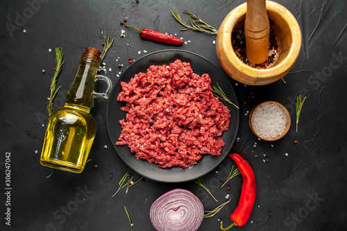 Fresh raw minced beef with herbs and spices on a black plate on a stone background