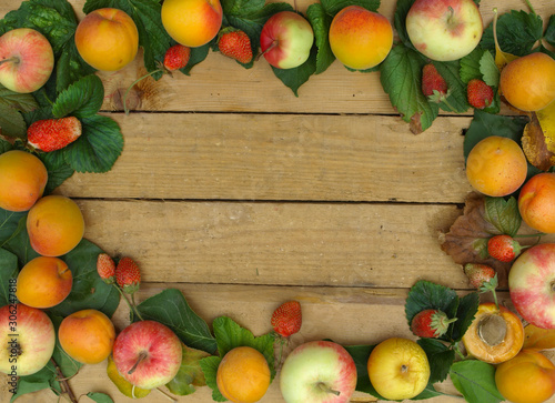 Frame of fruits and green leaves on a wooden background. Apricots and apples.
