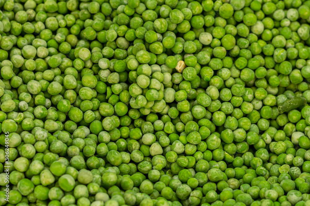 a lot of peeled green frozen peas. among it lies green beans.