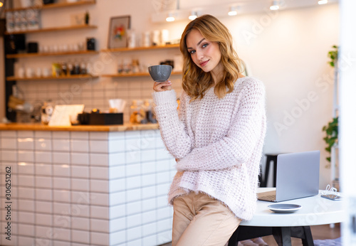 Happy young blonde woman posing in cafe drinking coffee
