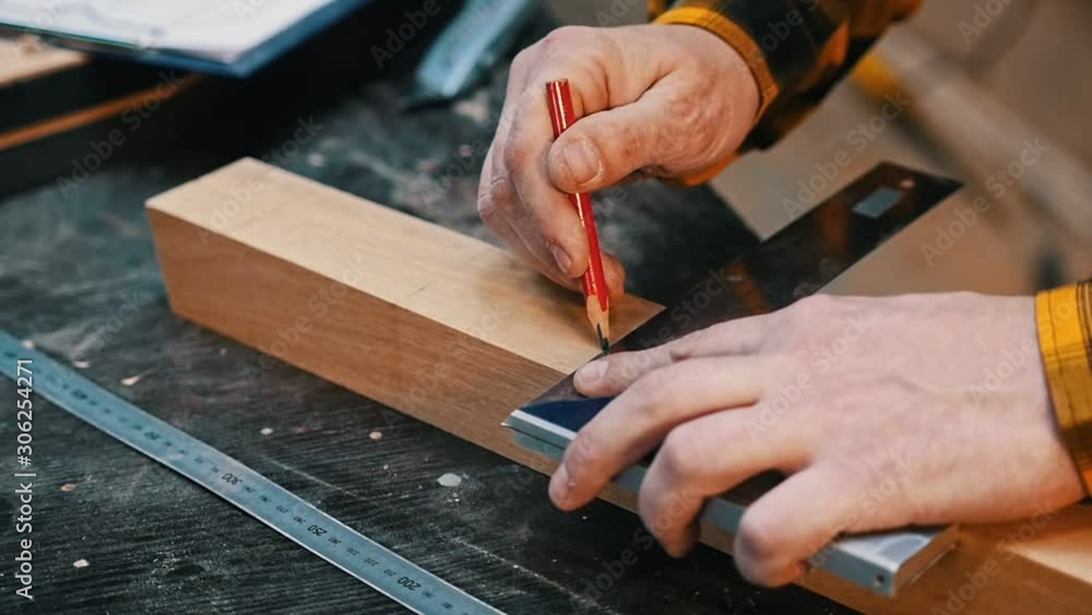 Carpentry industry - a man woodworker making marks for cutting on the wooden detail with a pencil Carpentry industry - a man woodworker making marks for cutting on the wooden detail with a pencil