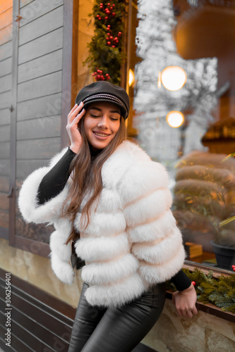 Obraz na płótnie Beautiful young caucasian woman wearing natural short white fur coat posing for a portrait near Christmas showcase. Christmas decor. Fashion. Style. Winter clothes made of natural fur. Vertical w salonie