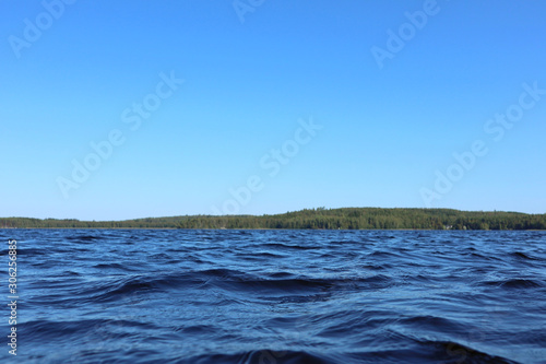 Blue water clear sky sunny day on finnish lake water waves close up. Beauty of nature skyline and forest with deep colored water. Photo from boat