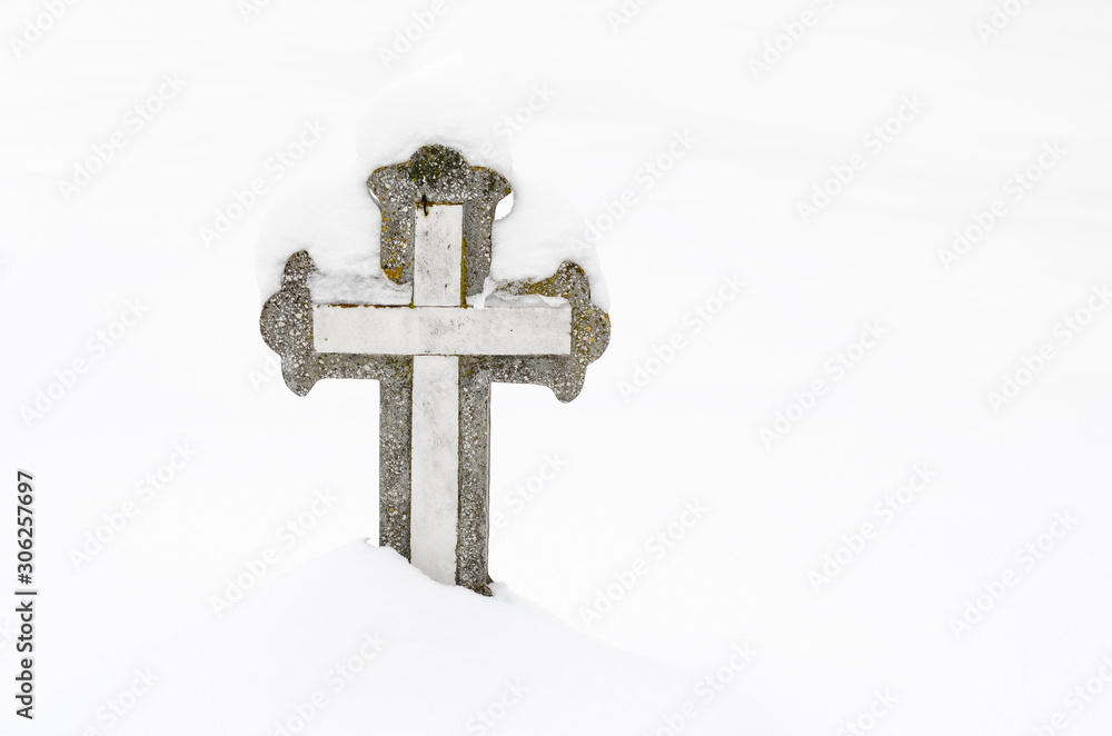 Christian stone cross in the cemetery, covered with snow .