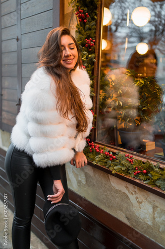 Obraz na płótnie Beautiful young caucasian woman wearing natural short white fur coat posing for a portrait near Christmas showcase. Christmas decor. Fashion. Style. Winter clothes made of natural fur. Vertical w salonie