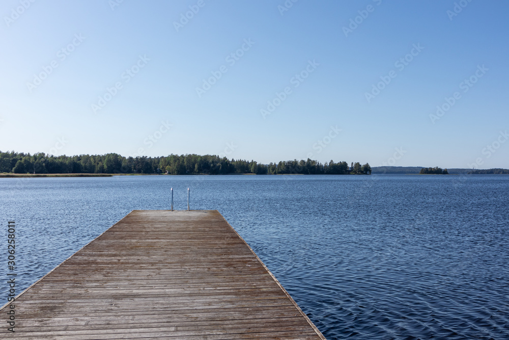 Wooden swimming dock pier with metal ladder on calm blue lake sunny day on nature finland idyllic natural resort