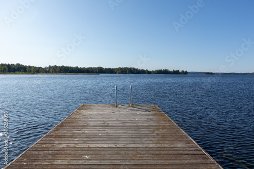 Wooden swimming dock pier with metal ladder on calm blue lake sunny day on nature finland idyllic natural resort
