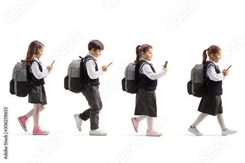 Three schoolgirls and one schoolboy with mobile phones walking in line