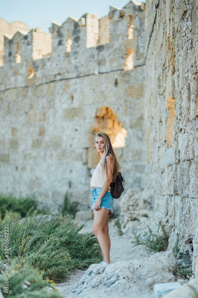 Beautiful young blonde hair girl traveler near the fort wall Rhodes island, Greece