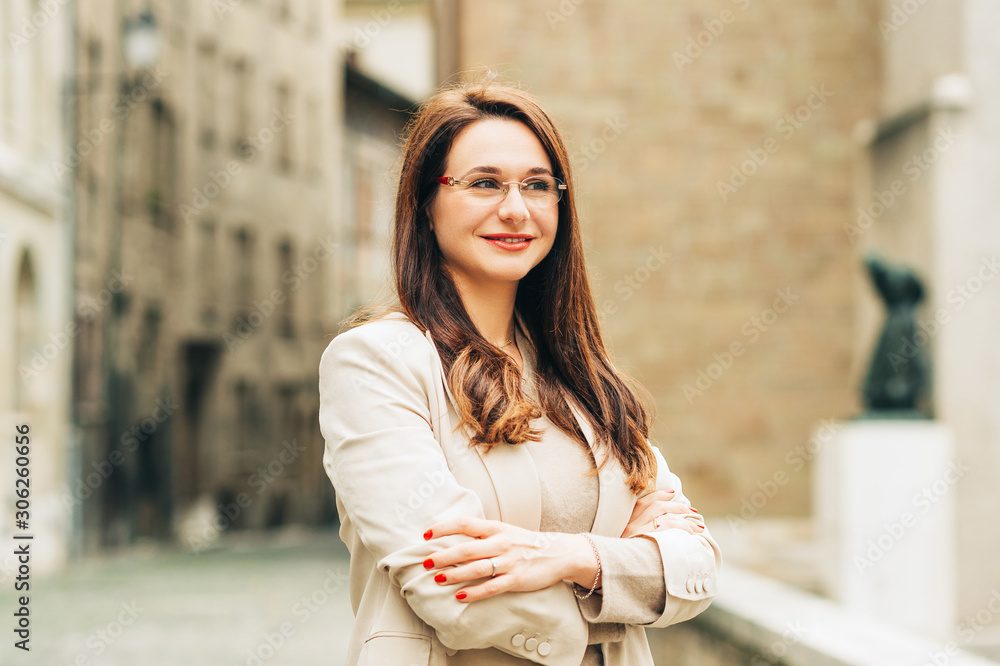 Outdoor portrait of beautiful woman posing on the city street, wearing beige suit and glasses