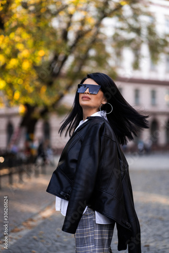 Autumn fashion outdoor. The girl in fashionable stylish white shirt , pants, jacket and sunglasses, autumnal lifestyle on the background of blurry yellow-green trees in the park. Vertical