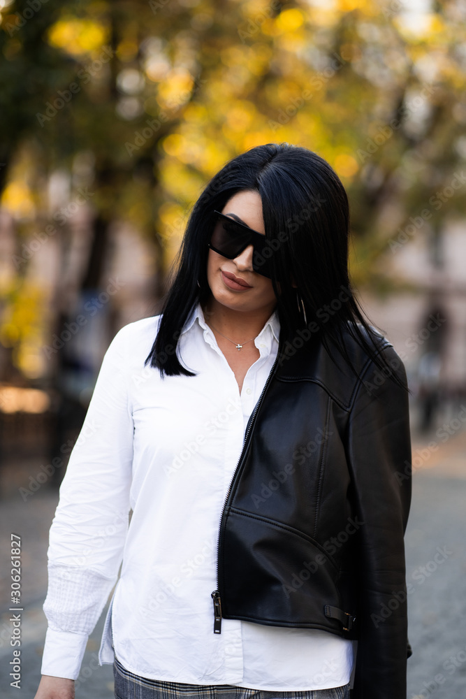 Autumn fashion outdoor. The girl in fashionable stylish white shirt , pants, jacket and sunglasses, autumnal lifestyle on the background of blurry yellow-green trees in the park. Vertical