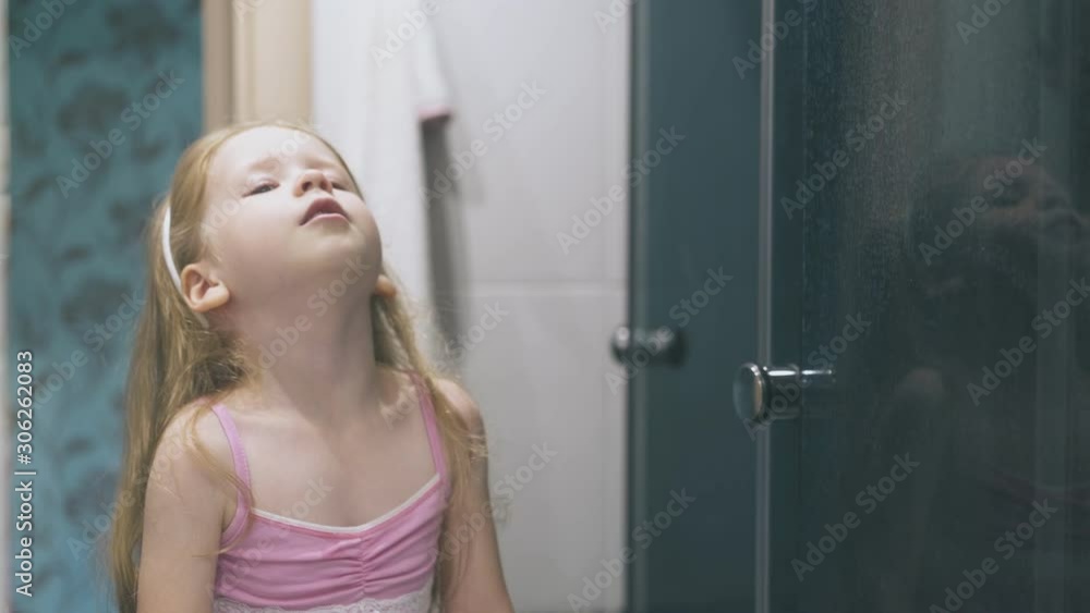 cute little girl with long hair in pink shirt gargles sore throat at large mirror in light bathroom at home cute little girl with long hair in pink shirt gargles sore throat at large mirror in light bathroom at home