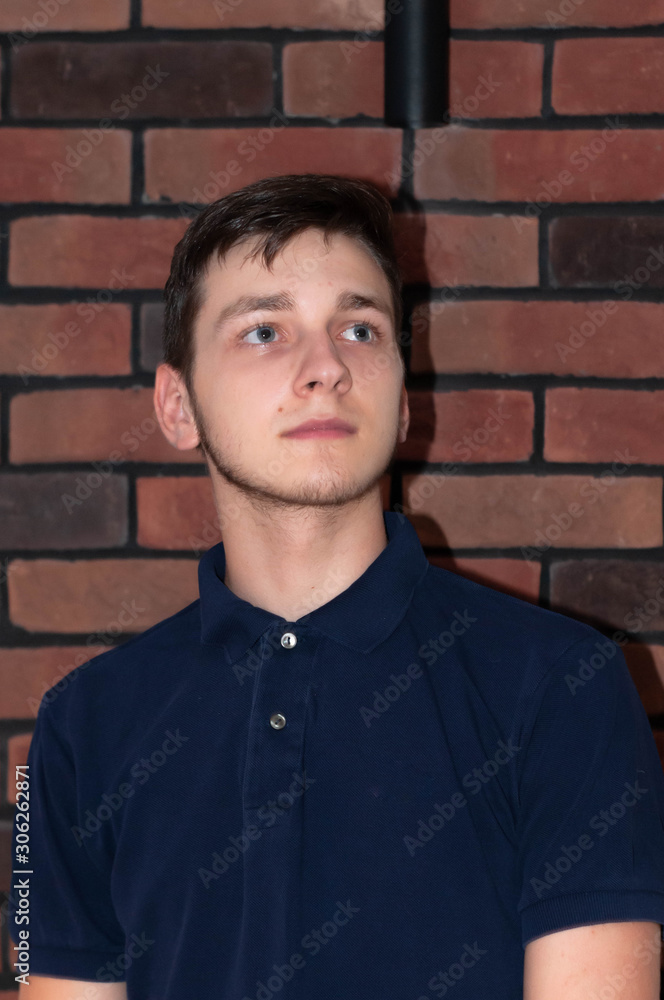 portrait of handsome young man in blue t shirt looking away in front of brick wall portrait of handsome young man in blue t shirt looking away in front of brick wall