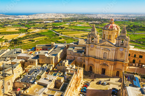 The main church and square in Mdina city - old capital of Malta. Aerial nature landscape  sunny day  blue sly  winter  a lot of green grass  field on background. Malta island