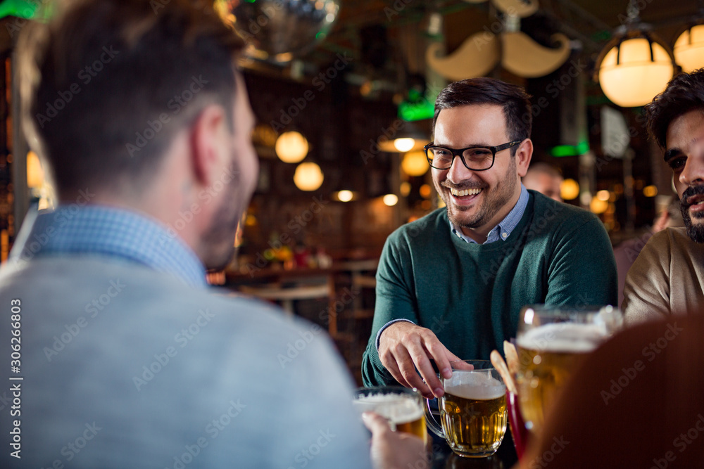 Handsome man drinking beer in pub with his friends