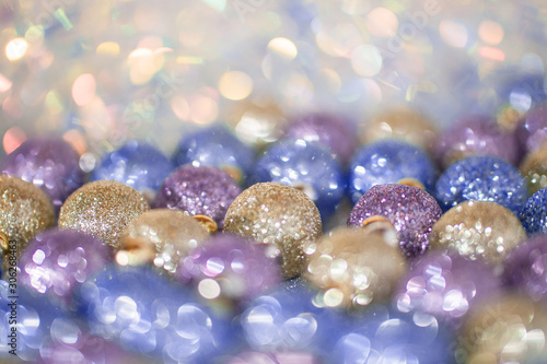 Blurred image of bright violet, blue and gold Christmas toys on sparkle background. Soft focus and beautiful bokeh.