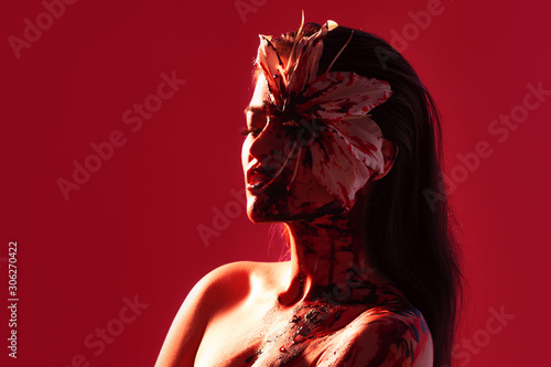 Blood Lily, scary and sexy Halloween look. Beautiful young brunette girl on red background.