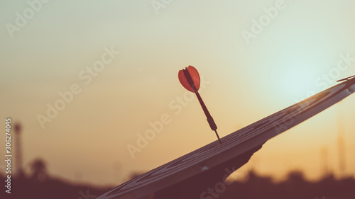 Close up red dart arrow hitting target center dartboard on sunset background. Business targeting and focus concept