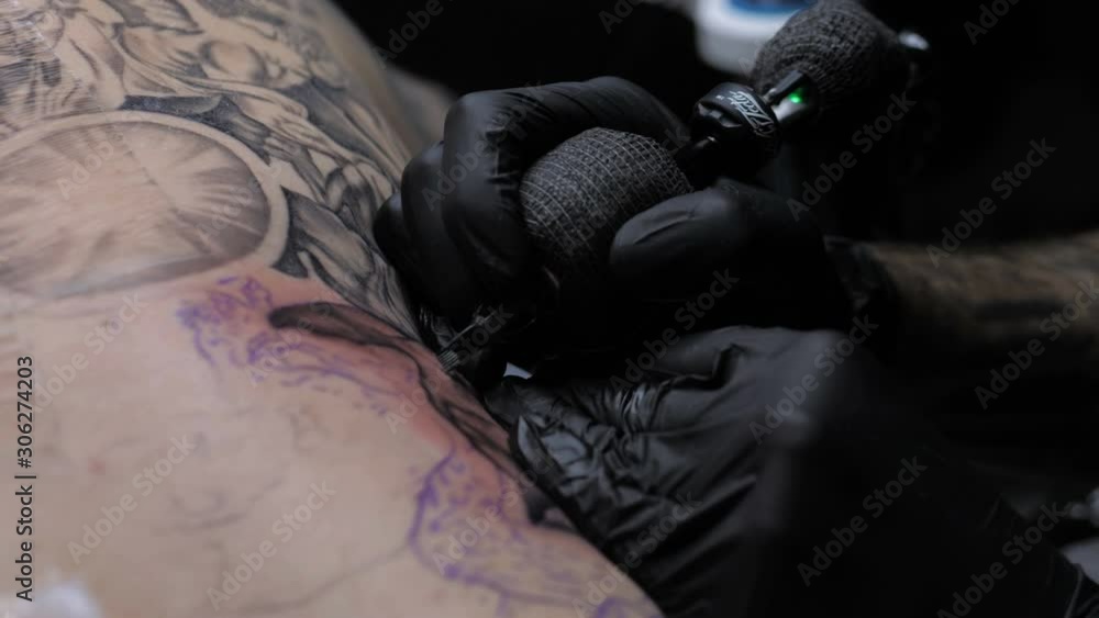 Close up tattoo artist demonstrates the process of getting black tattoo with paint on back of a client Close up tattoo artist demonstrates the process of getting black tattoo with paint on back of a client