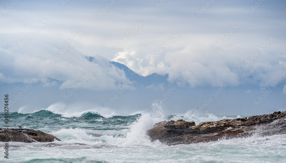 Sea landscape. Clouds sky, waves with splashes, mountains silhouettes. False bay. South Africa.