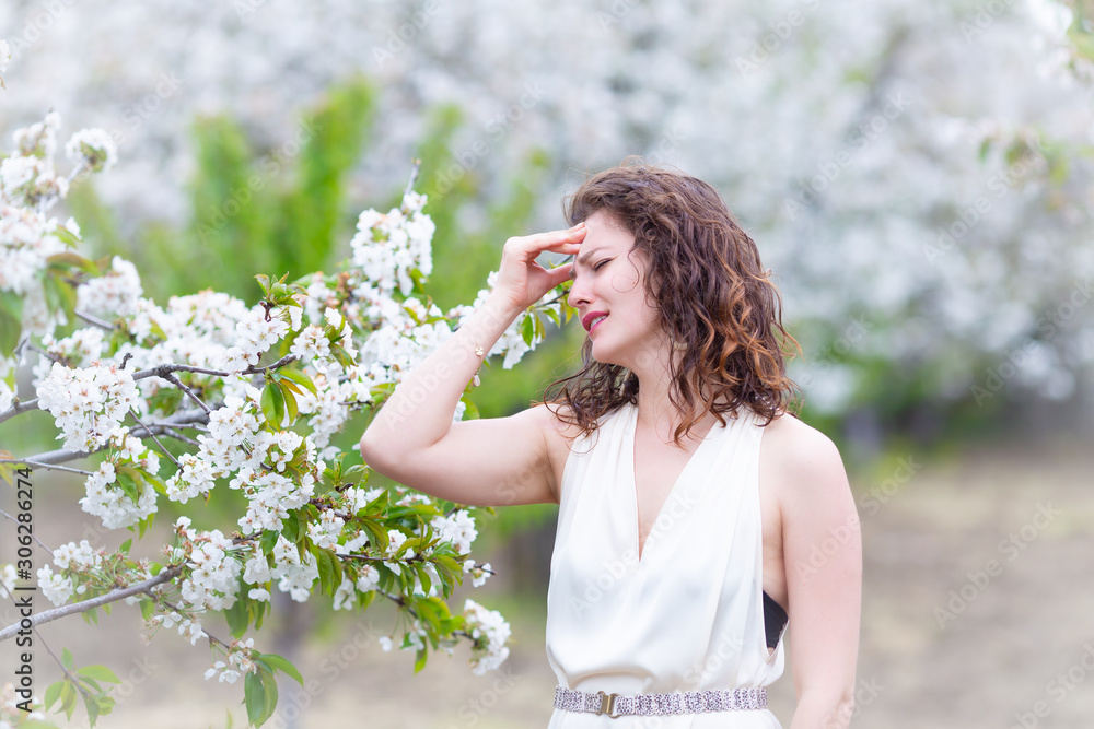 A portrait of Caucasian brunette woman near blossoming cherry tree. Painful emotions, headache A portrait of Caucasian brunette woman near blossoming cherry tree. Painful emotions, headache