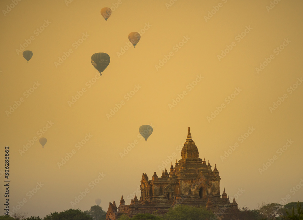 Sunrise with dusty smoke and many hot air balloons above The Bagan Archaeological Zone in Myanmar.