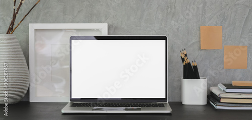 Modern workplace with open blank screen laptop computer and office supplies on black table and grey wall