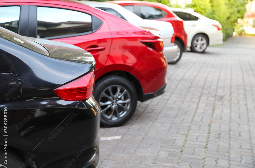 Closeup of rear, back side of black car with  other cars parking in outdoor parking area  with natural background in bright sunny day. 