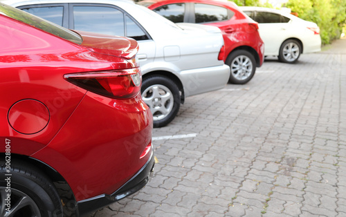 Closeup of rear, back side of red car with other cars parking in outdoor parking area with natural background in sunny day. 
