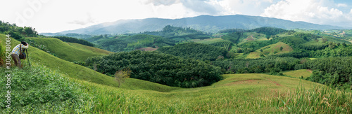 Photographer with a camera and tripod on green natural valley. Panorama view