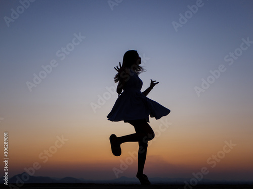 Silhouette of a young dancing woman with long wavy hair in the mountains , Natural light and darkness,against the background of the sunset sky.