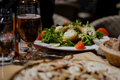 Goat cheese salad on table with beer and other delicious itens out in the sun, blurred foreground. Colmar, Alsace