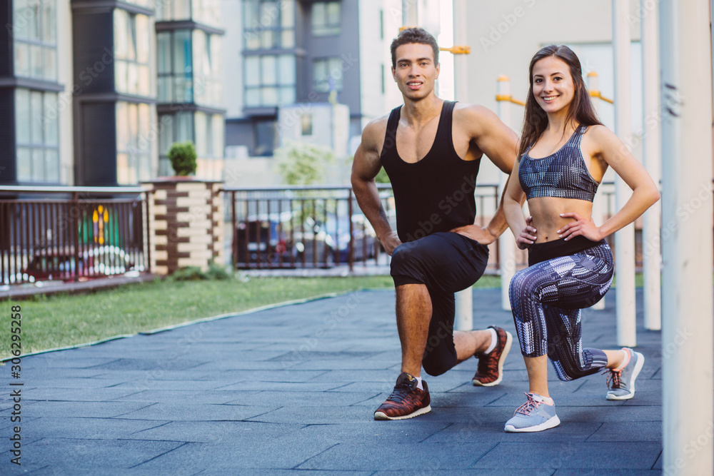 Smiling positive sporty caucasian woman dressed in sportswear, Mixed race man with ponytail doing lunges in outdoor gym.