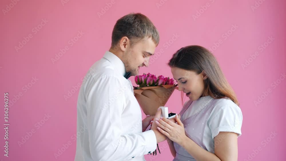 Man in elegant clothing is giving flowers and ring to happy young woman smiling, girl is expressing happiness. People, relationship and commitment concept. Man in elegant clothing is giving flowers and ring to happy young woman smiling, girl is expressing happiness. People, relationship and commitment concept.