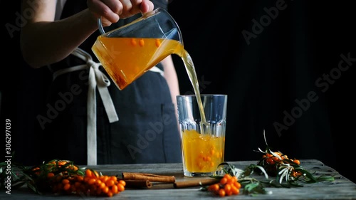 Herbal sea buckthorn tea pouring from glass teapot into the glass. Seamless cinemagraph looped video