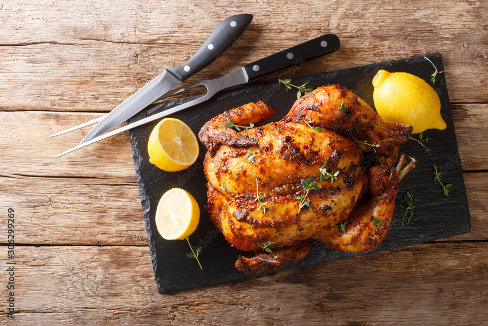 Traditional rotisserie chicken served with lemon closeup on a slate board on a table. Horizontal top view