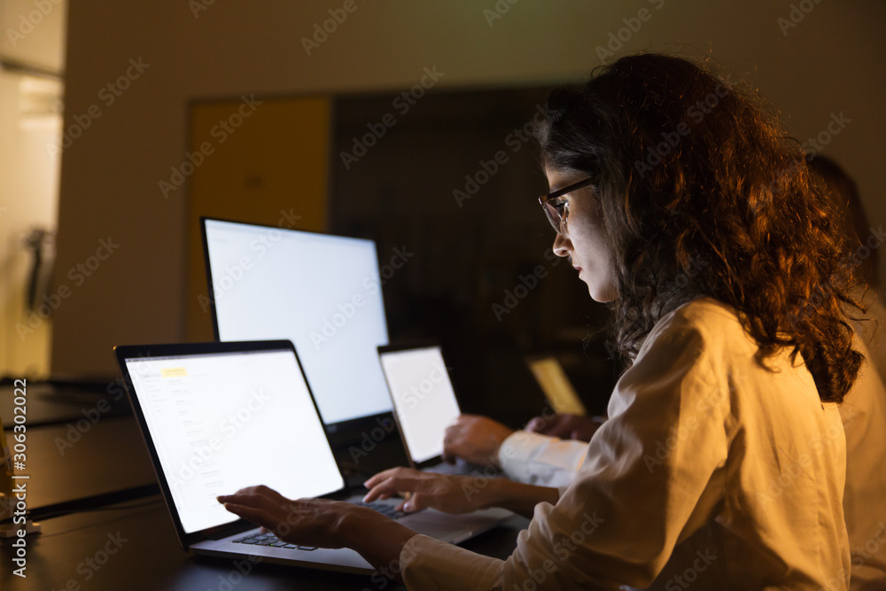 Business people using computers in dark office. Professional male and female business colleagues using laptops with illuminated screens late at night. Working late concept Business people using computers in dark office. Professional male and female business colleagues using laptops with illuminated screens late at night. Working late concept
