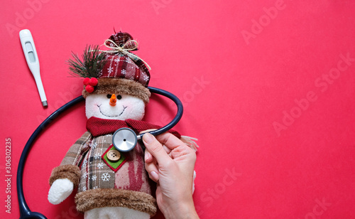 Doctor and christmas concept. Sick snowman and stethoscope on red background with place for text.