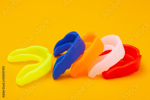 five colored boxing mouth guards laid out in a row on a yellow background, concept photo