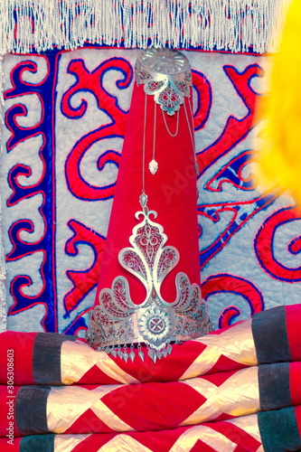 Kazakh yurt. Saukele - the bride's headdress lies on a pile of blankets on the background of an ornamented carpet. photo