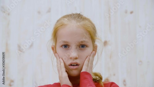 Surprised girl with opened mouth and eyes touching face front camera on light background. Shocked teenager girl from amazement holding face to hands. People emotion concept photo