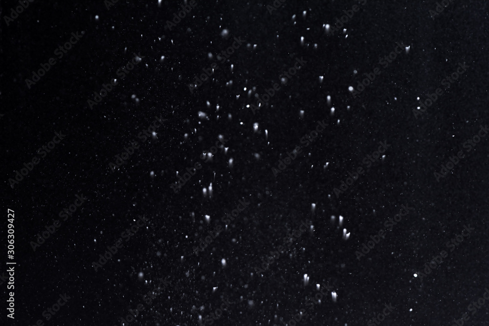 Fototapeta premium Falling snow at night. Bokeh lights on black background, flying snowflakes in the air. Overlay texture. Snowstorm