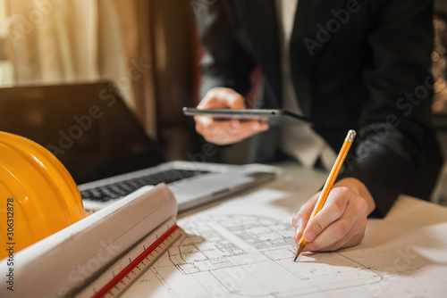 Businessman use tablet, laptop searching for data working with on on architectural project at construction site at desk in office.