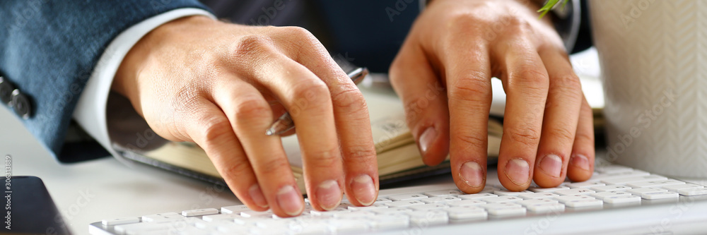 Male arms in suit typing on silver keyboard