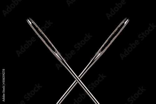 2 crossed large eye sewing needles on a black background.  High contrast and stron highligts in the steel.  Room for copy. photo