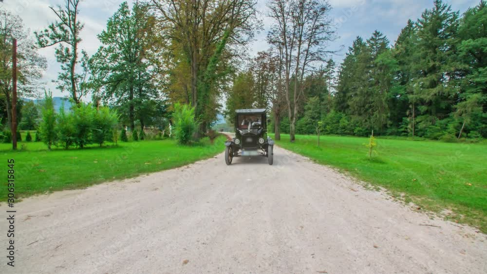 A slow-motion dynamic dolly shot of a black vintage car driving through a path surrounded by nature. A slow-motion dynamic dolly shot of a black vintage car driving through a path surrounded by nature.