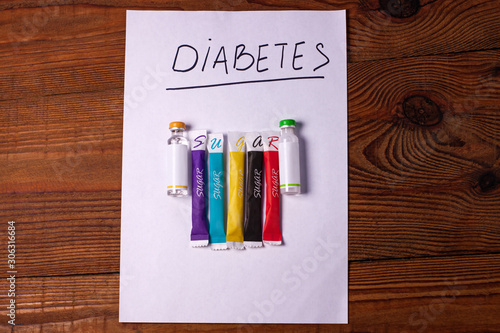 Diabetes sign on a white paper with insulin ampoules, colorful sugar sticks on wooden background, World diabetes day concept.Prevent disease before it begins,detection diagnosis, patients list mockup. photo