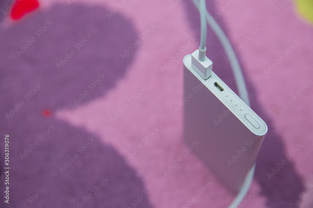 Fototapeta premium Energy bank . Smartphone Charging with silver Power Bank Through Spiral USB Cable . Smartphone charging with power bank on pink carpet .